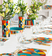 Vista Alegre | Futurismo Charger Plate featuring bold geometric patterns, set on a white tablecloth with gold-tone cutlery and lily centerpieces for a stylish dining experience.