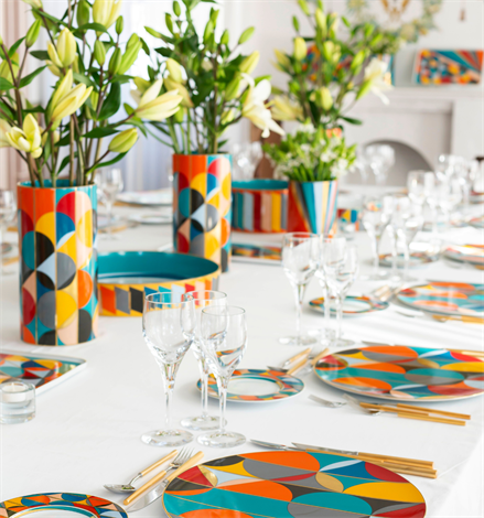 Vista Alegre | Futurismo Charger Plate featuring bold geometric patterns, set on a white tablecloth with gold-tone cutlery and lily centerpieces for a stylish dining experience.