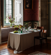 Dining corner featuring Vista Alegre | The Meaning XL Plate on a linen-draped table with fruit bowl, green glass vessels, and elegant tableware, set against historic decor.