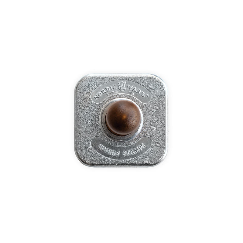 Nordic Ware | Gingerbread cookie stamp featuring a round metal design with a brown wooden handle, perfect for creating festive holiday cookies.