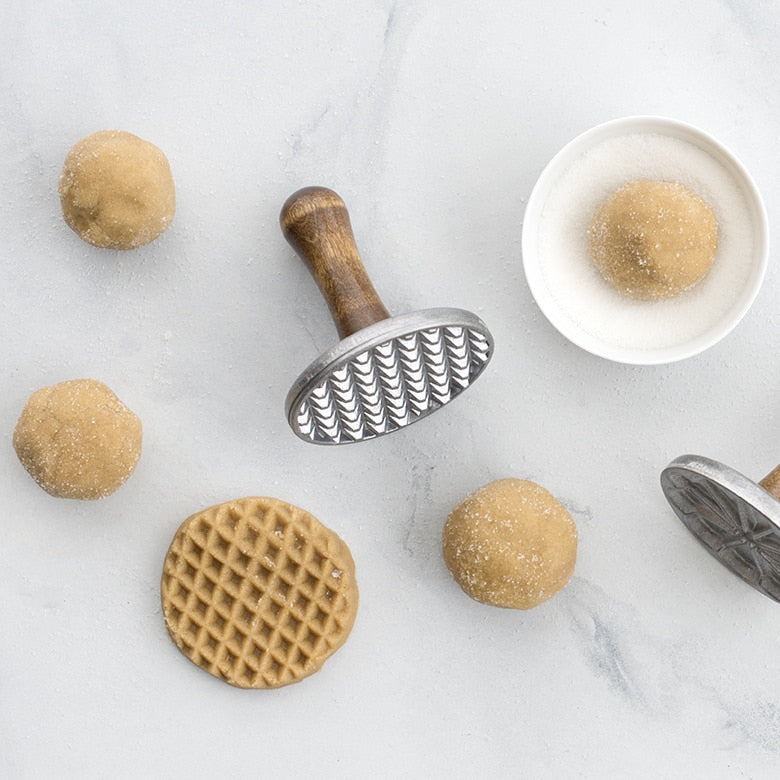 Nordic Ware | Heirloom Cookie Stamps pressing patterns into dough, showcasing flower, scallop, and diamond textures for homemade cookie creations.