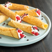Nordic Ware | Norwegian Krumkake and Pizzelle Iron displayed with dessert pastries on a plate, showcasing the tool's versatility in creating intricate, traditional cookies.