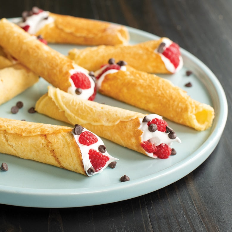Nordic Ware | Norwegian Krumkake and Pizzelle Iron displayed with dessert pastries on a plate, showcasing the tool's versatility in creating intricate, traditional cookies.