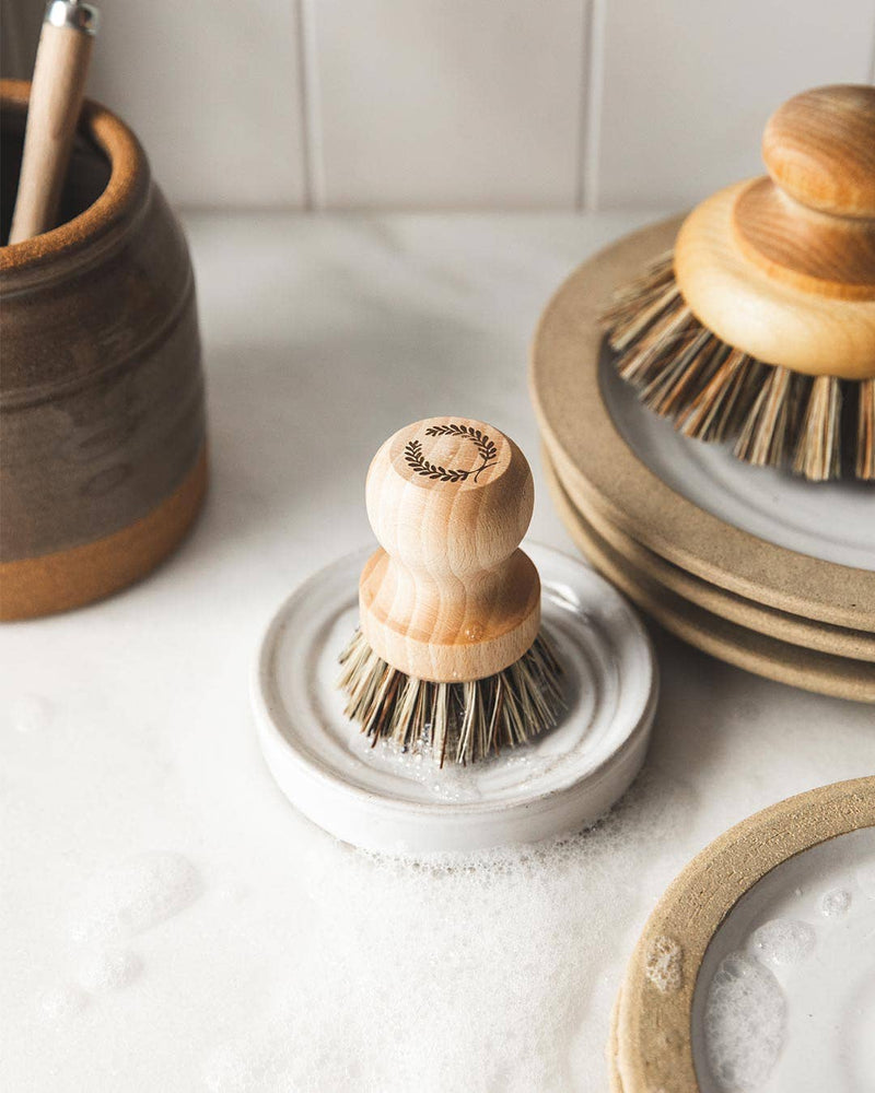 Farmhouse Pottery - Laurel Pot Brush Set in a sudsy dish, surrounded by wooden utensils and stoneware plates, ideal for efficient kitchen cleanup.