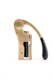 L'Atelier du Vin - USA - Lever Wine Opener - OENO MOTION GOLD NOMAD features a brushed brass finish with a black leather grip, showcasing elegant craftsmanship.