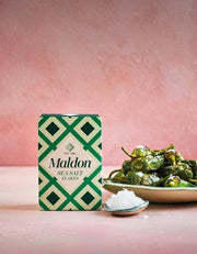 Wholesome Good - Maldon Sea Salt 8.5oz / 12: Single, showcased with a ceramic spoon and blistered peppers, highlighting its culinary appeal for gourmet cooking.