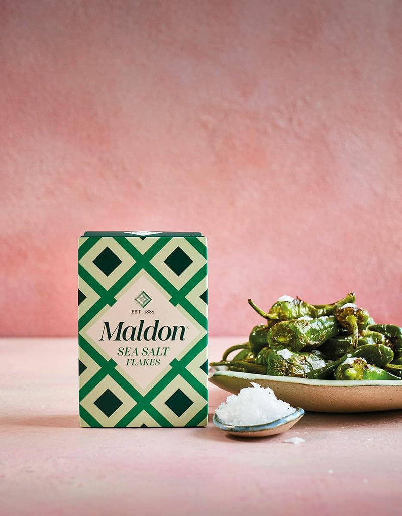 Wholesome Good - Maldon Sea Salt 8.5oz / 12: Single, showcased with a ceramic spoon and blistered peppers, highlighting its culinary appeal for gourmet cooking.