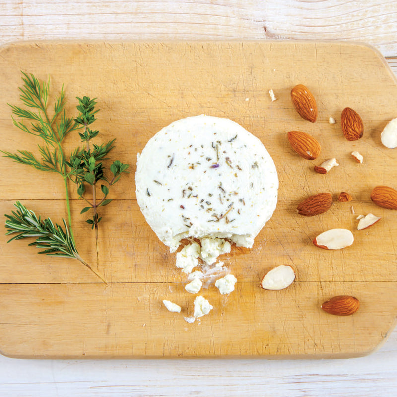 Cypress Grove | Herbs de Humboldt Goat Cheese on a wooden board, showcasing a round, herb-coated cheese with a creamy white interior.