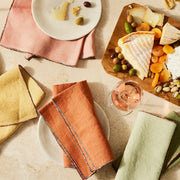 Overhead view of a casual cheese-and-wine spread featuring Atelier Saucier's Mix-and-Match Chroma Napkins in muted tones, styled with white plates and a wooden serving board.