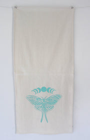 Hearth and Harrow - Organic Cotton Luna Moth Tea Towel featuring a screen-printed moth and moon phases design, displayed against a white wall. Eco-friendly and handcrafted.