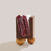 Atelier Saucier | Les Trois Wooden Napkin Holder featuring a dark walnut box on birch wood legs, with colorful textiles draped over its U-shaped opening.