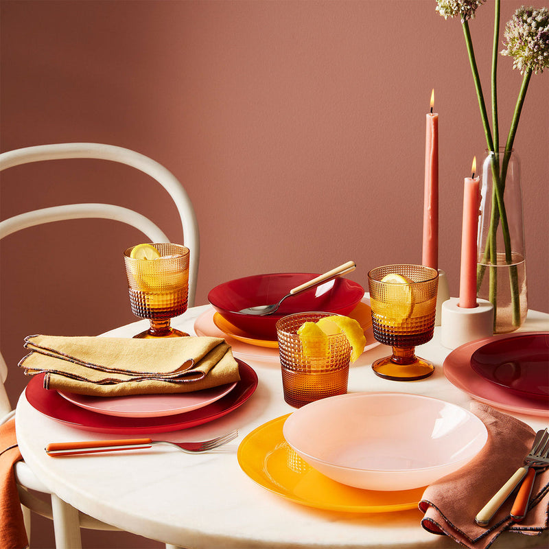 Atelier Saucier Mix-and-Match Chroma Napkins, Set of 6, displayed on a colorful dinnerware table setting with textured amber glass tumblers and lit taper candles.
