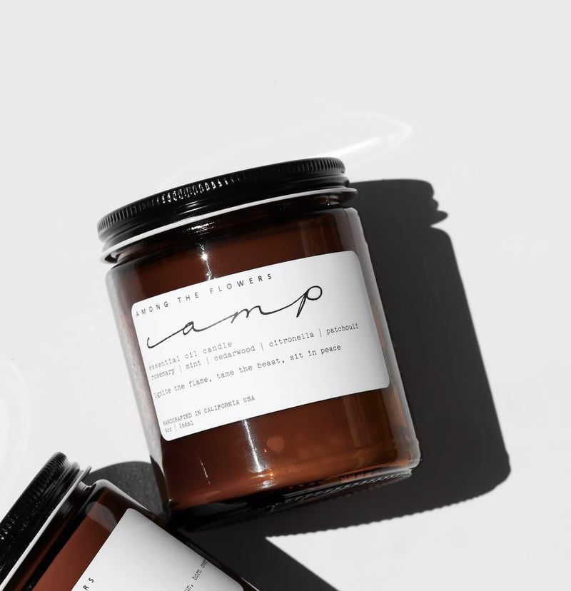 Among the Flowers | Essential Oil Candle, Through the Woods: amber glass jar with black lid, featuring rosemary, mint, cedarwood, citronella, and patchouli scent.
