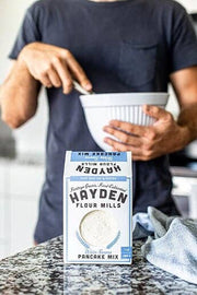 Person making pancakes with Hayden Flour Mills - White Sonora Pancake Mix on a kitchen countertop, showcasing simple preparation with minimal ingredients.