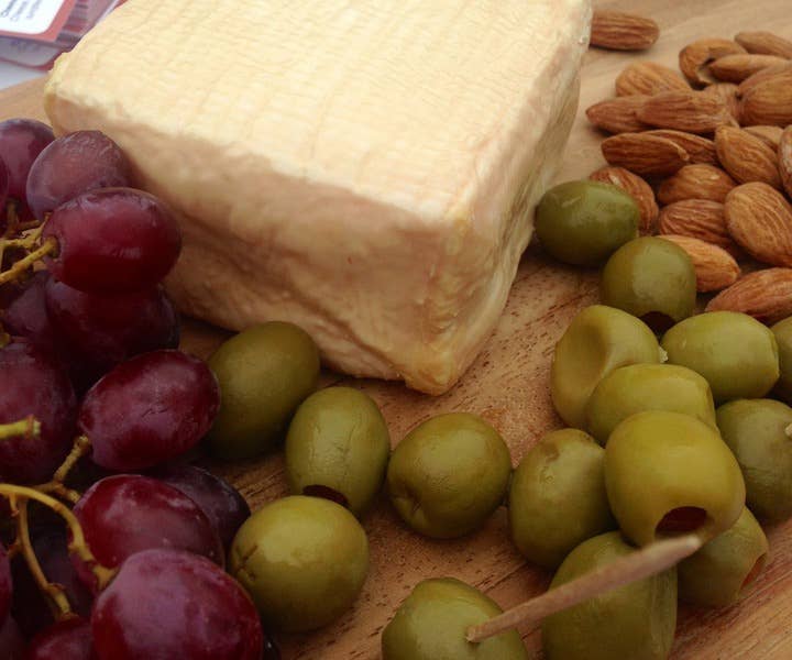 Tulip Tree Creamery - Foxglove cheese with grapes on a wooden surface, showcasing its soft, scoopable texture and distinctive orange rind.