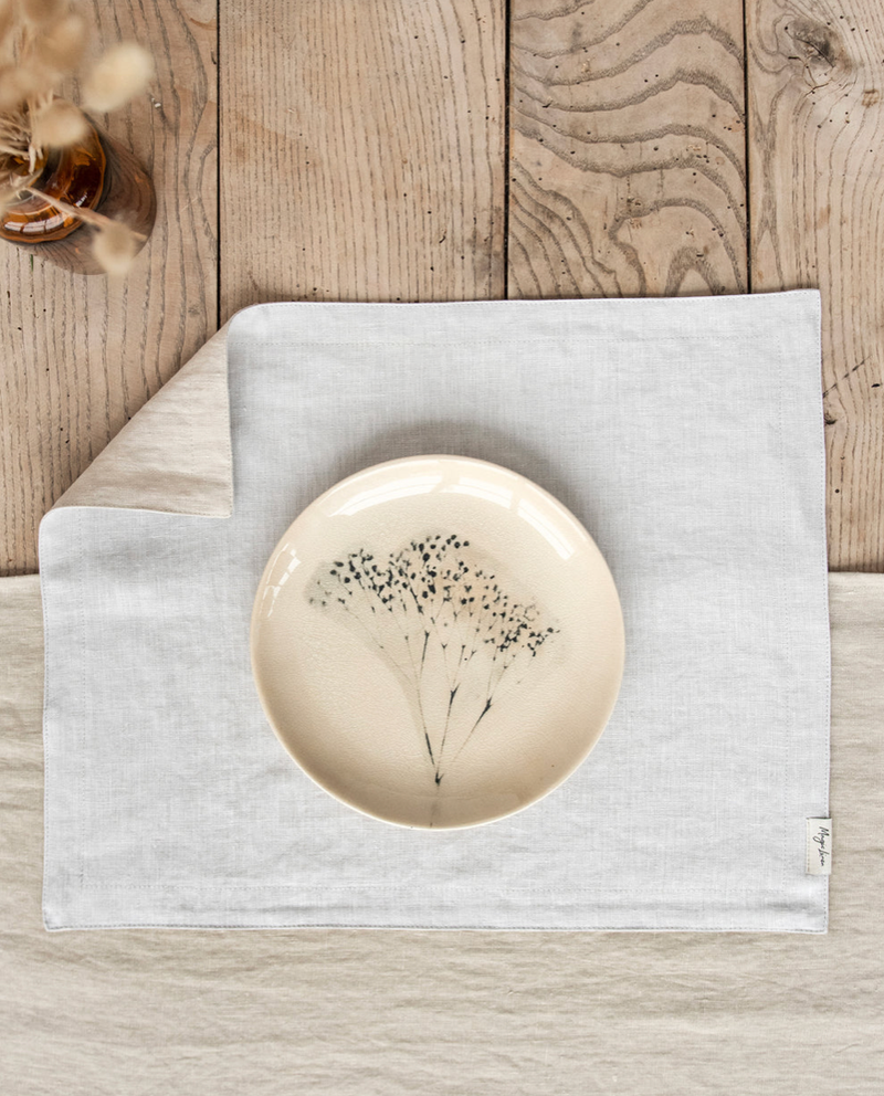 MagicLinen double layer linen placemat set of 2 in light grey displayed under a floral-design plate on a wood surface, showcasing texture and style.