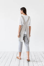 MagicLinen Pinafore cross-back linen apron with twin-sectioned pocket, showcased by a model in casual attire, ideal for cooking and gardening.