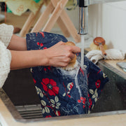 Hands washing Bee's Wrap - Bread Wrap - Botanical Print under running water with a brush, showcasing its reusability and sustainability for bread storage.