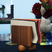 Atelier Saucier | Les Trois Wooden Napkin Holder: Dark walnut block with birch spheres, elegantly holding cloth napkins, set on a styled table with decorative elements.