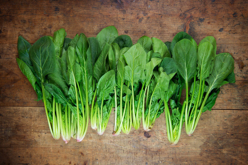 Bentley Seed Co. - Spinach-Bloomsdale Savory 1820: Fresh spinach bunches on wooden surface, ideal for salads or smoothies, grown from heirloom seeds.