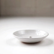 Gravesco Pottery Incense Burner, a minimalist white ceramic dish, features a central peg for incense sticks, designed to catch ash efficiently.