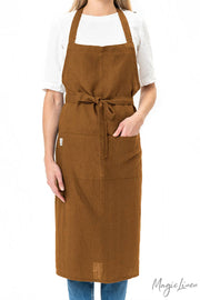 Person wearing MagicLinen's Charcoal Grey Linen Bib Apron with Pockets, showcasing its stylish and functional design ideal for cooking or gardening.