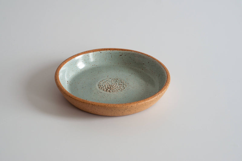 RachaelPots - Garlic Scraper: Nude/White, a handcrafted ceramic dish with a pale greenish-blue speckled glaze interior and terracotta exterior, ideal for transforming garlic cloves into puree.