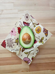 Avocado half on Bee's Wrap - Assorted 3 Pack - Meadow Magic, Plant-Based Wax, showcasing reusable, vegan-friendly food preservation on a wood tabletop.