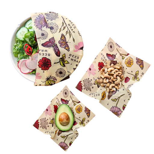 Bee's Wrap - Assorted 3 Pack - Meadow Magic, featuring botanical-butterfly prints, covers a salad bowl, holds cashews, and wraps half an avocado. Eco-friendly, plant-based, reusable.