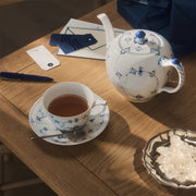 Royal Copenhagen | Blue Fluted Pl Teapot 100cl with blue floral motifs, surrounded by matching teacup, rock-sugar bowl, and gift tags on a wooden table.