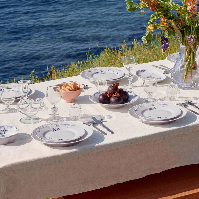 Royal Copenhagen | Blue Elements Plate, 22cm, set on a terrace table with blue floral motifs, surrounded by glassware and wildflower bouquet overlooking water.
