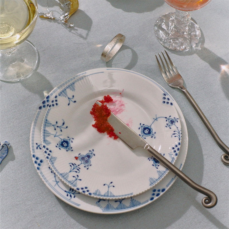 Royal Copenhagen | Blue Elements Plate, 22cm, featuring hand painted blue floral patterns, stacked with a butter knife and caviar, elegantly set on a dining table.