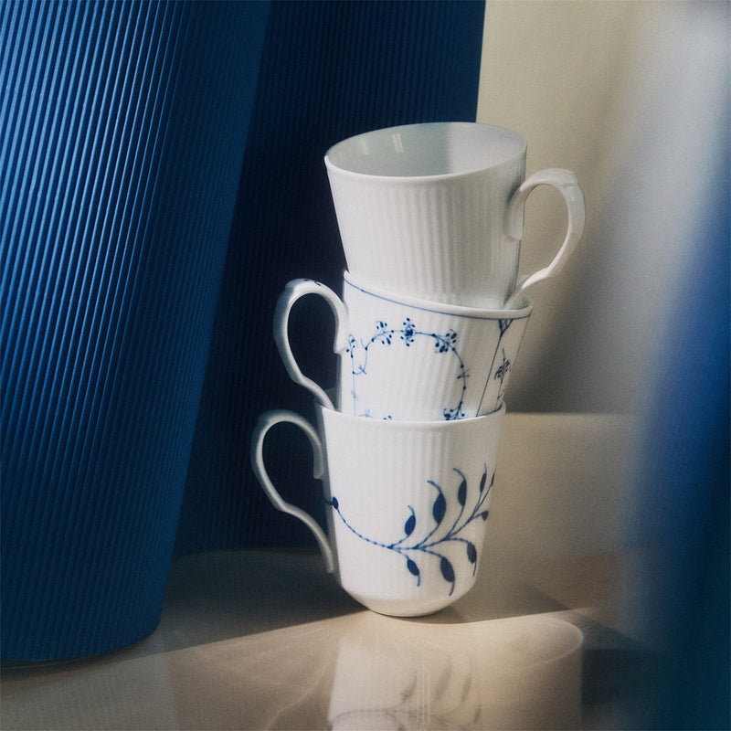 Royal Copenhagen | Gifts With History Cups, Set of 3, featuring stacked blue-floral and vine-patterned porcelain mugs, elegantly displayed with blue decorative vases in the background.