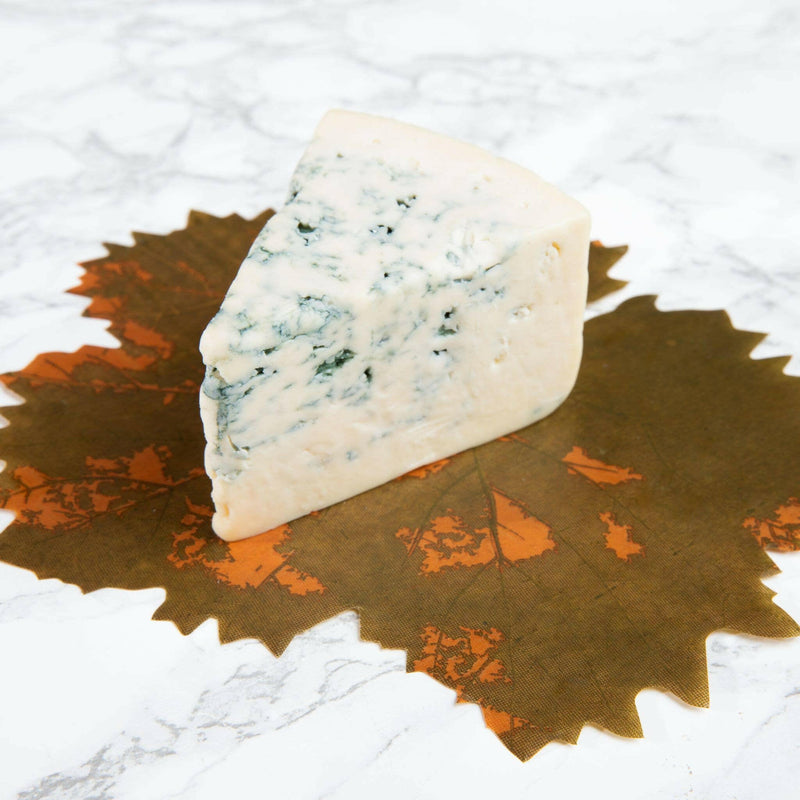 Formaticum | Cheese Board Liners - Large displayed on a leaf, showcasing wax-coated parchment with a grape leaf design, ideal for elegant culinary presentations.