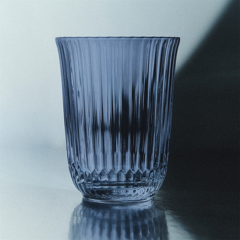 Royal Copenhagen | Waves Highball Glass, Blue, featuring vertical ribbing, on a reflective surface, showcasing modern elegance and perfect for summer drinks or cocktails.
