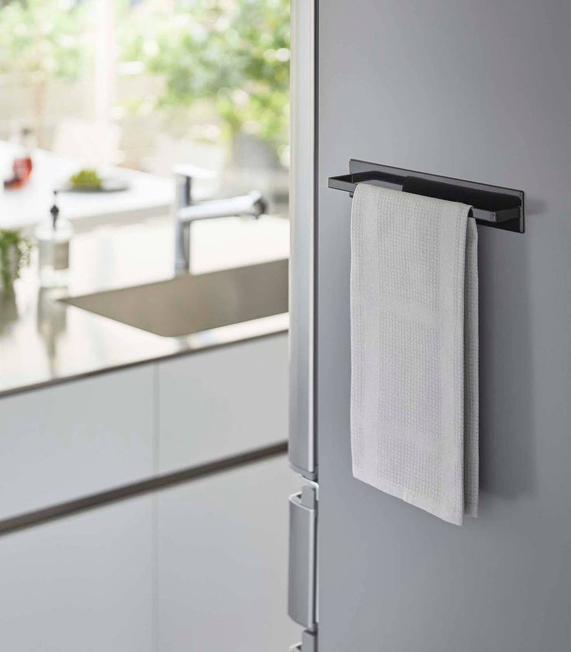 Yamazaki Home - Magnetic Kitchen Towel Hanger - Steel: White, attached to a stainless-steel fridge, holding a white waffle-weave towel, enhancing kitchen organization.