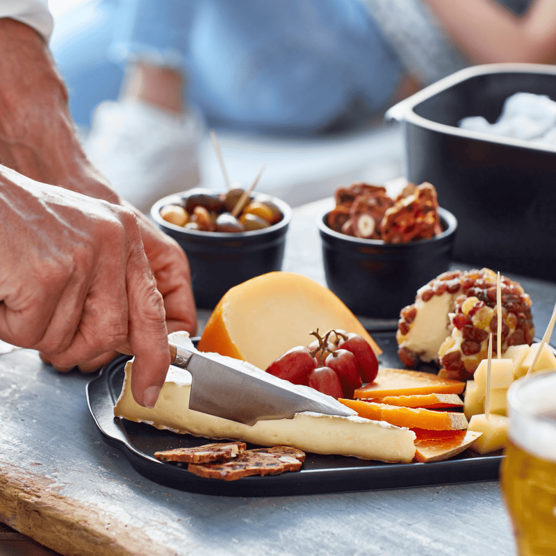 Emile Henry Cheese Box showcased with assorted cheeses, grapes, crackers, and olives, highlighting its versatile serving platter lid and practical design for cheese enthusiasts.