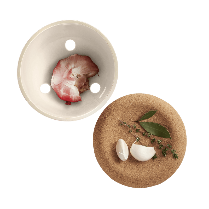 Emile Henry | Garlic Pot, Truffle, displayed with garlic cloves, bay leaves, and thyme on a cork trivet, showcasing its elegant, vented ceramic design for freshness.