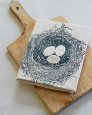 Hearth and Harrow - Nest Tea Towel - Organic Cotton - Bird's Nest - Dark Blue, displayed on a cutting board, features an eco-friendly navy design and hanging loop.