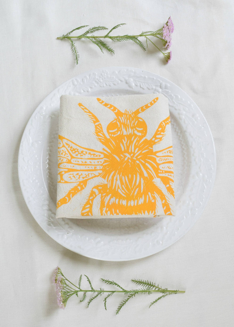 Hearth and Harrow - Honeybee Tea Towel in Yellow, featuring a bee design on organic cotton, eco-friendly and hand-printed, displayed elegantly on a dining plate.