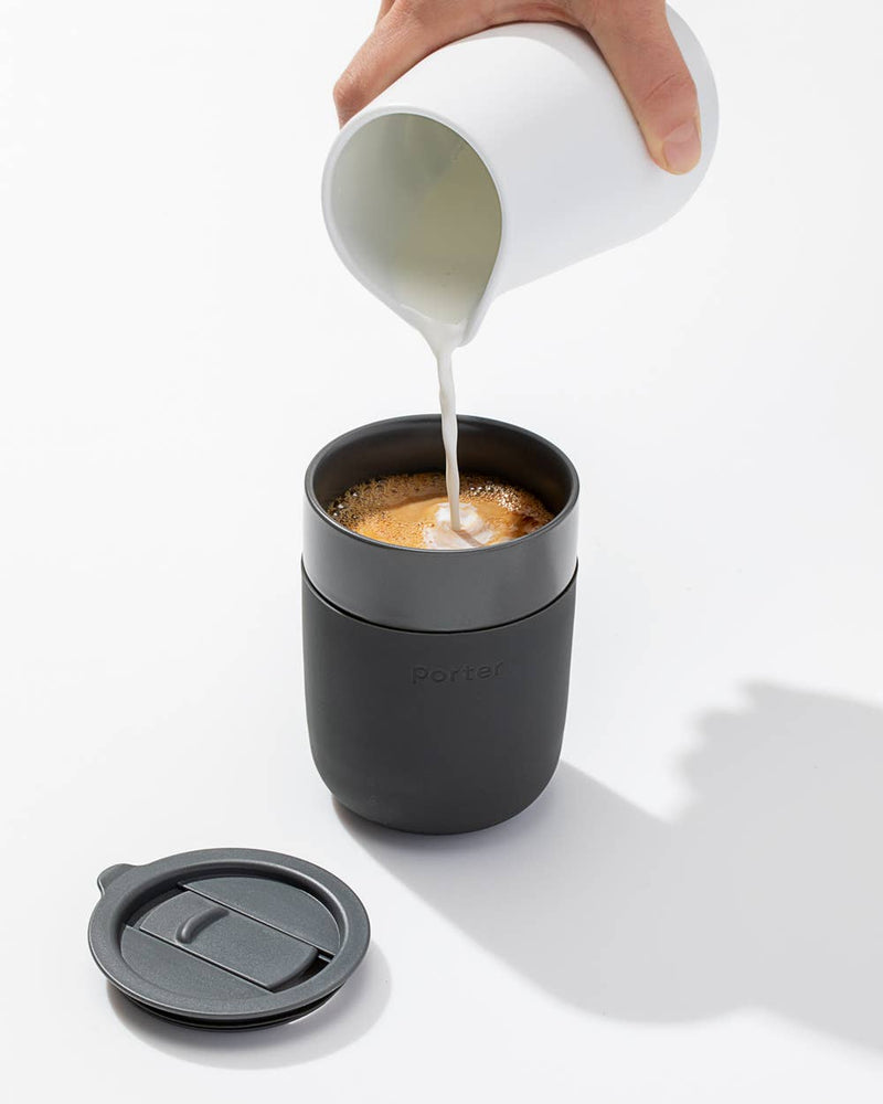 Person pouring milk into W&P - Reusable Ceramic Mug: Terrazzo Blush, featuring a splash-resistant lid and silicone sleeve, ideal for eco-friendly coffee enjoyment.