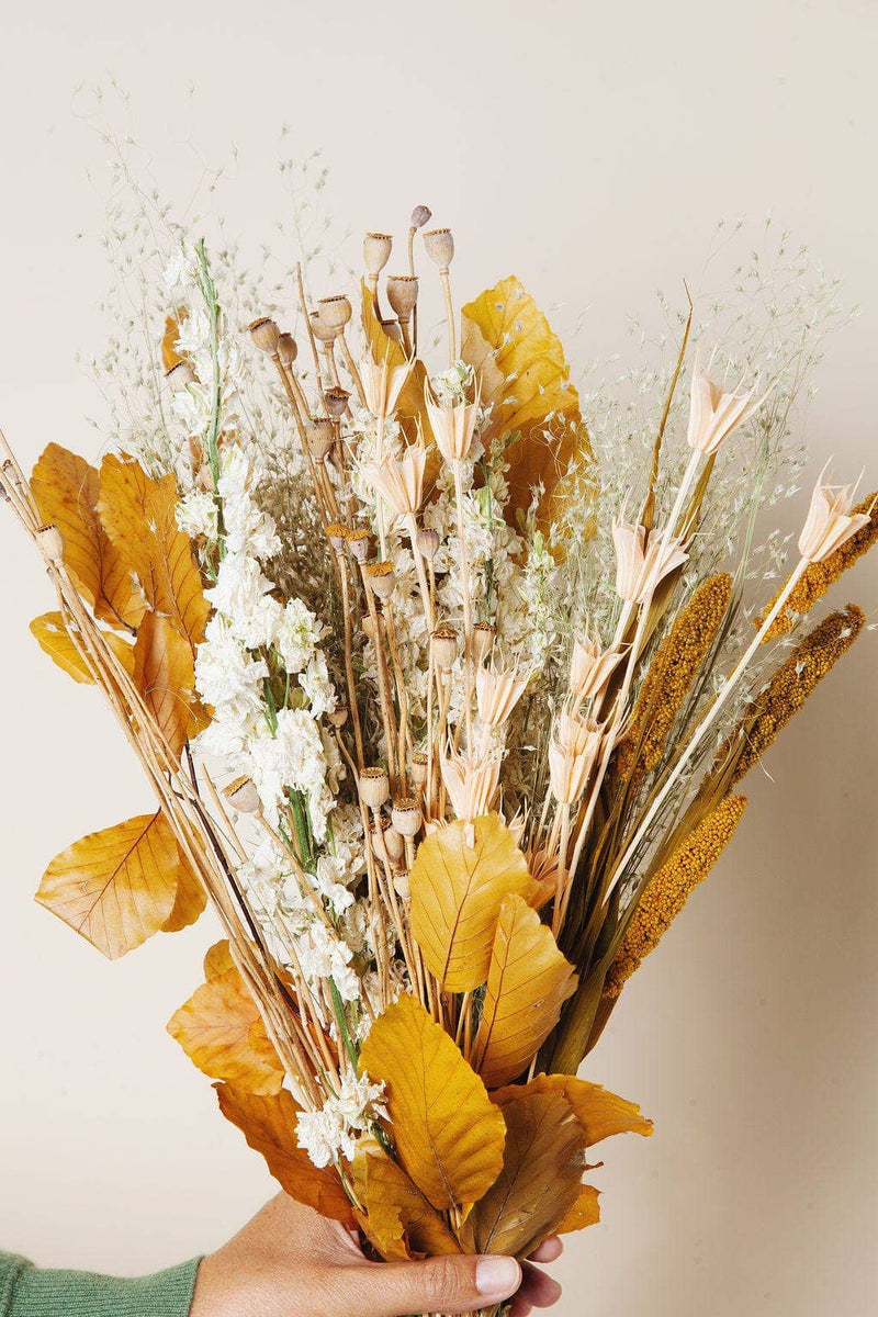 Idlewild Floral Co. - Golden Fall Market Bouquet: A hand holds a dried bouquet with autumn leaves, grasses, and blooms, perfect for lasting decorative beauty without maintenance.