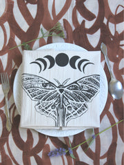 Hearth and Harrow - Organic Cotton Luna Moth Tea Towel with moon phases, elegantly set on a table, showcasing its eco-friendly design and fine dining appeal.