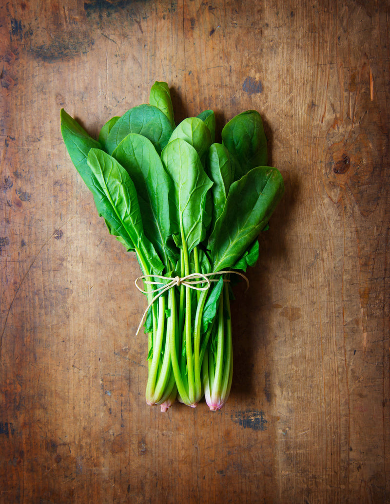 Bentley Seed Co. - Spinach-Bloomsdale Savory 1820: Fresh bunch of heirloom spinach leaves with stems tied with twine on a rustic wood surface, ideal for kitchen use.