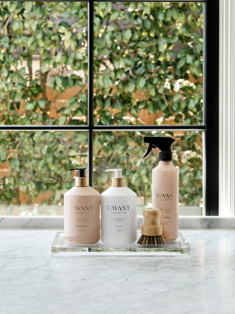 L'AVANT Collective - Multipurpose Surface Cleaner - Blushed Bergamot bottles on a counter with a wooden brush, highlighting eco-friendly packaging and plant-based cleaning formula.