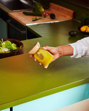 Hand holding Holcomb Studio Totter Salad Dressing Shaker, with a bowl of salad nearby, showcasing a mustard-like yellow liquid inside the jar.