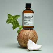 Davids Hydroxi™ oil pulling oral rinse bottle balanced on a coconut with mint, highlighting its natural ingredients and oral health benefits.