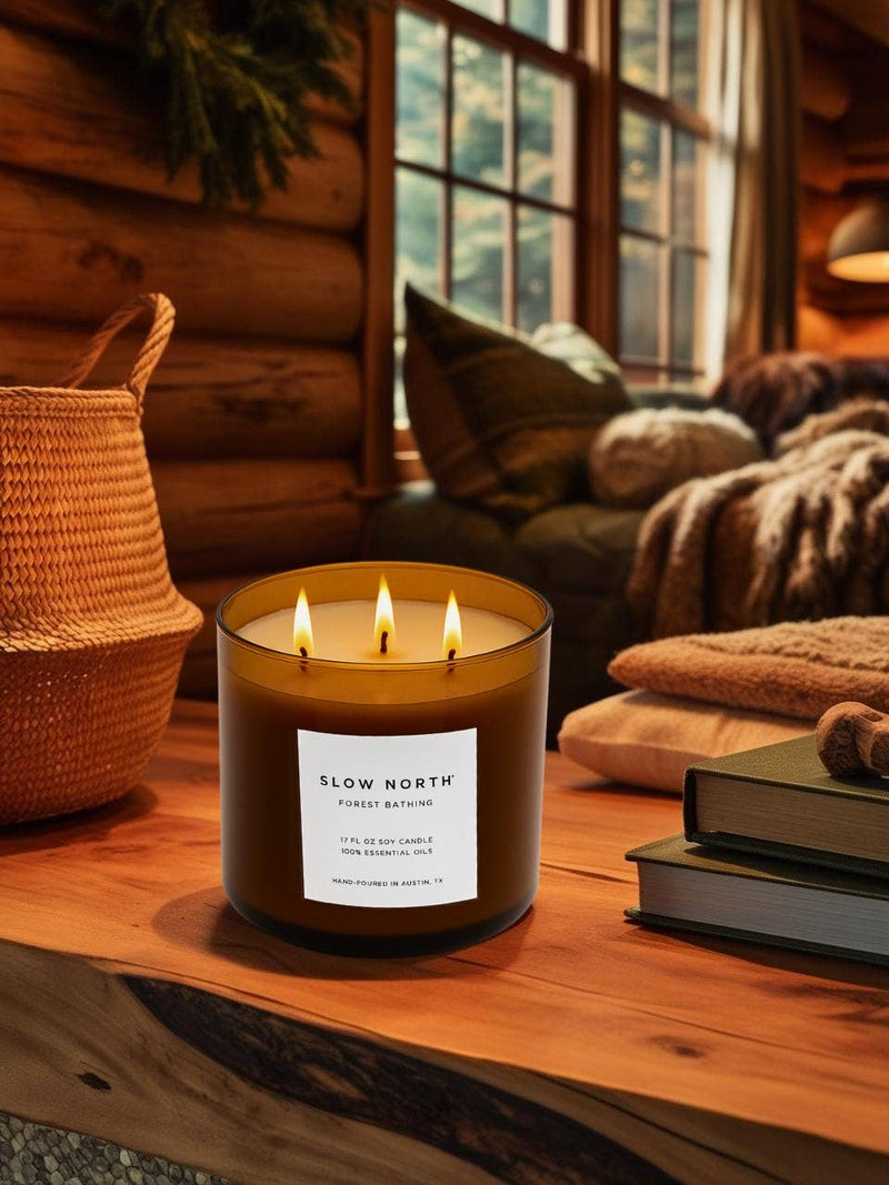 Slow North - Forest Bathing 3-Wick Soy Candle with essential oils on a wooden surface, casting a warm glow, surrounded by cozy cabin decor.