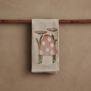 Coral & Tusk - Mushroom Tea Towel with embroidered toadstool and ferns on natural linen, draped over a wooden rod. Perfect for adding whimsy to your kitchen.