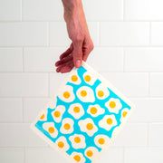 Bespoke Provisions - Eggs Swedish Dishcloth held over a napkin, showcasing its design and highlighting its utility for cleaning tasks.